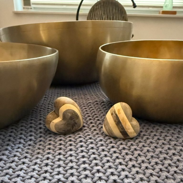 Drei große Klangschalen und zwei herzförmige Steine auf einer gewebten Decke.