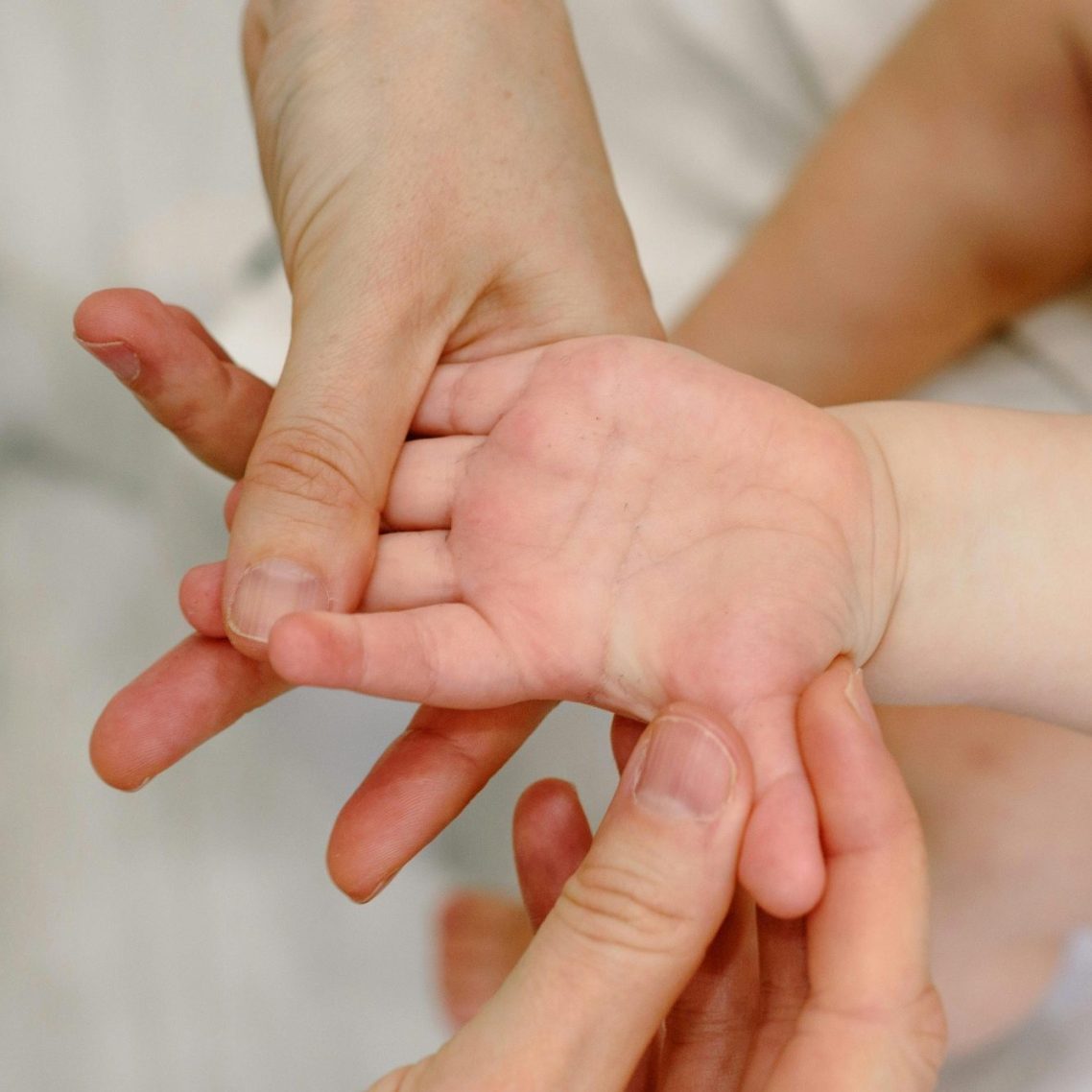 Eine Erwachsene Hand hält eine kleine Kinderhand und massiert diese sanft.